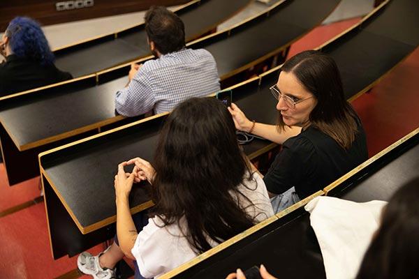 Students seated in an auditorium having a conversation before class begins.