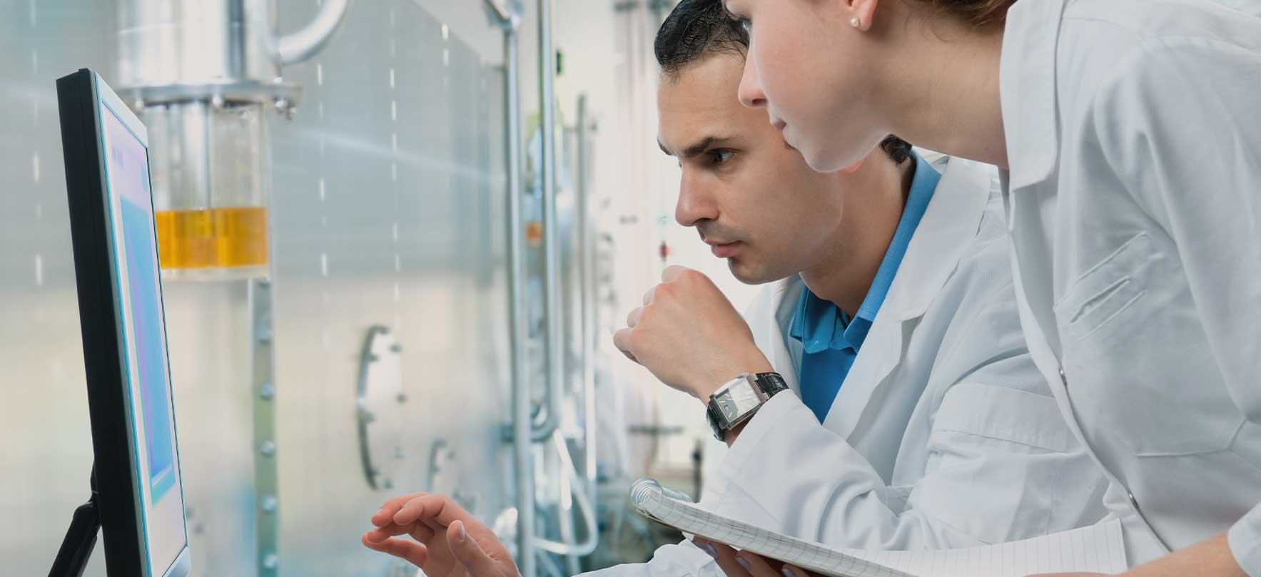 Two researchers in lab coats analyzing data on a computer screen in a laboratory setting.